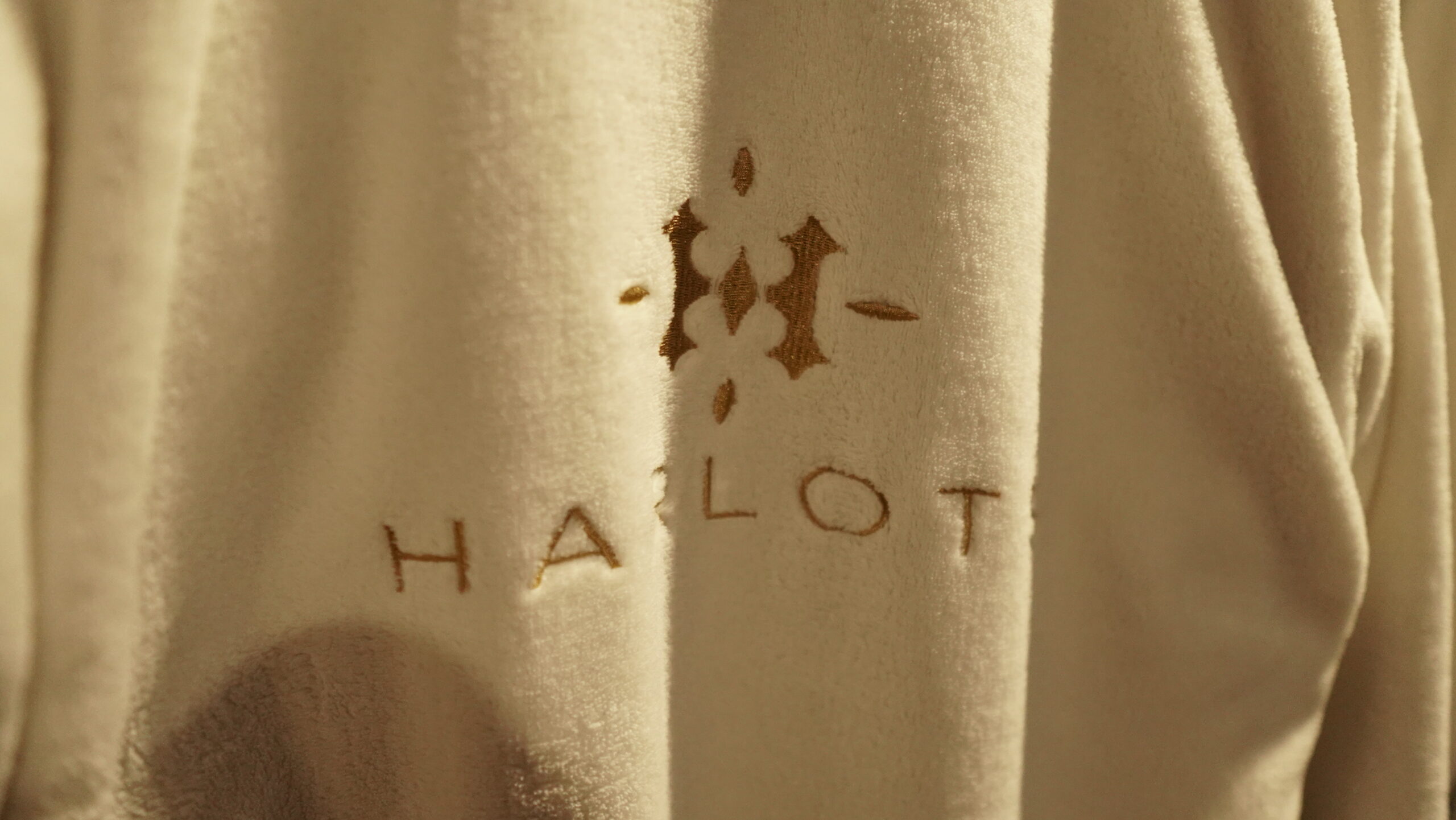 Close-up of a plush white bathrobe embroidered with the gold Harlots logo and crest