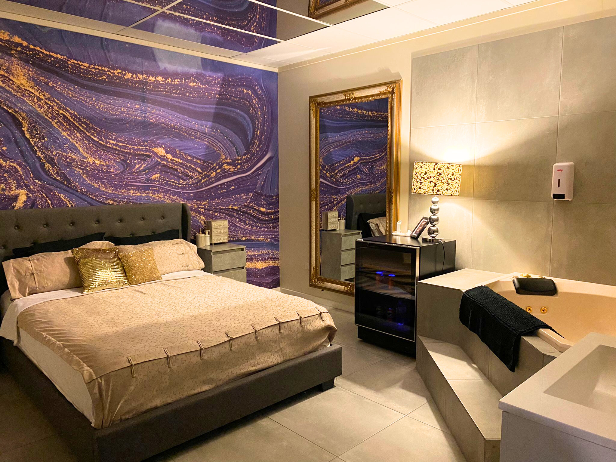 visiting a Harlots brothel Luxury private suite at Harlots featuring a plush bed with gold cushions, purple abstract wall mural, large floor mirror, and corner spa tub.